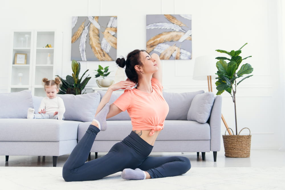 Hábitos saudáveis durante a quarentena: mãe fazendo yoga e a filha no sofá.